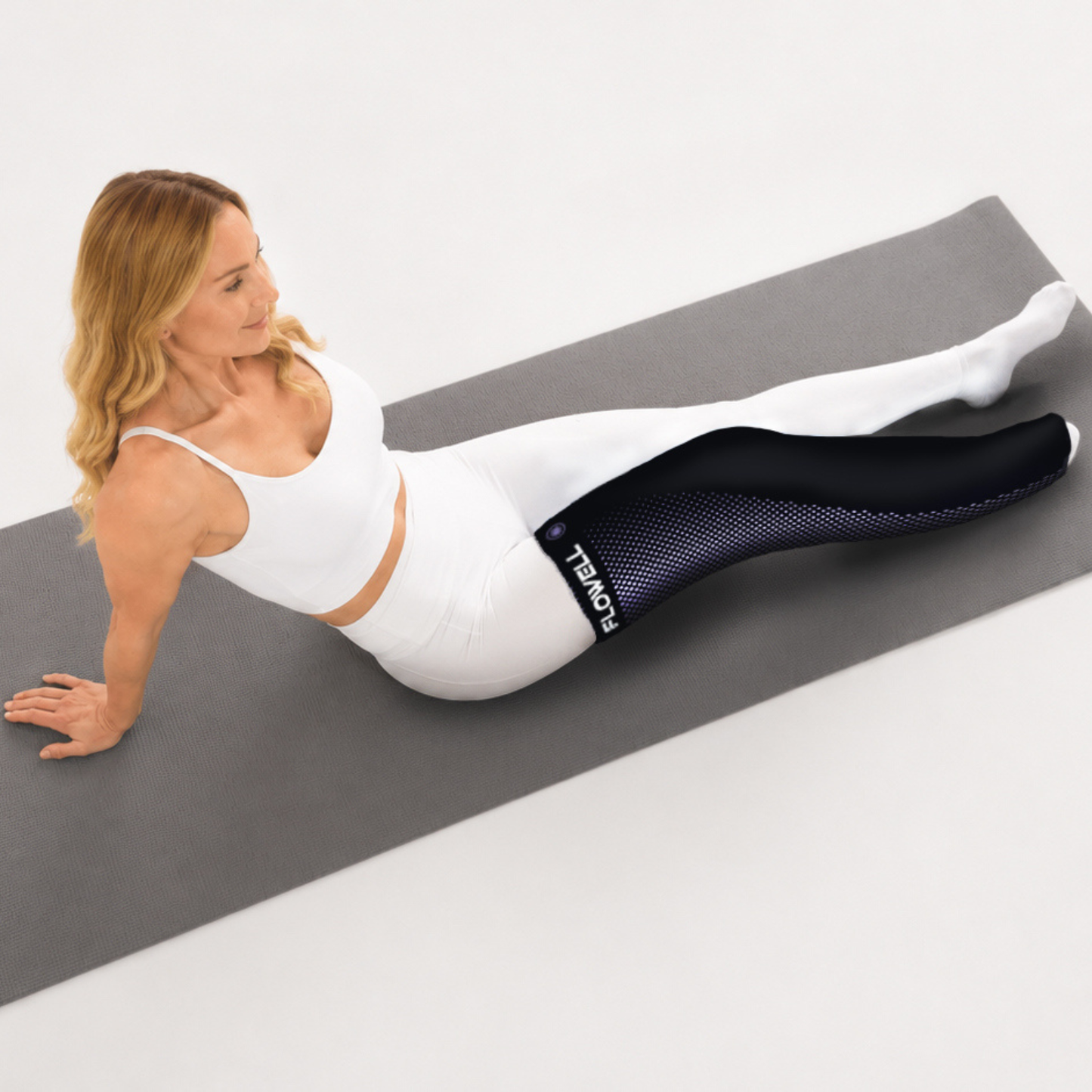 Flowell: Woman exercising on a gray mat wearing black leggings with a visible brand logo.
