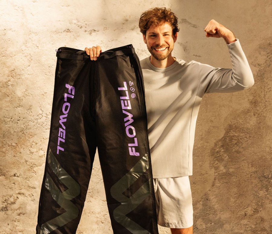 Flowell - Man holding his Sport Deluxe pants with a smile against a textured wall.