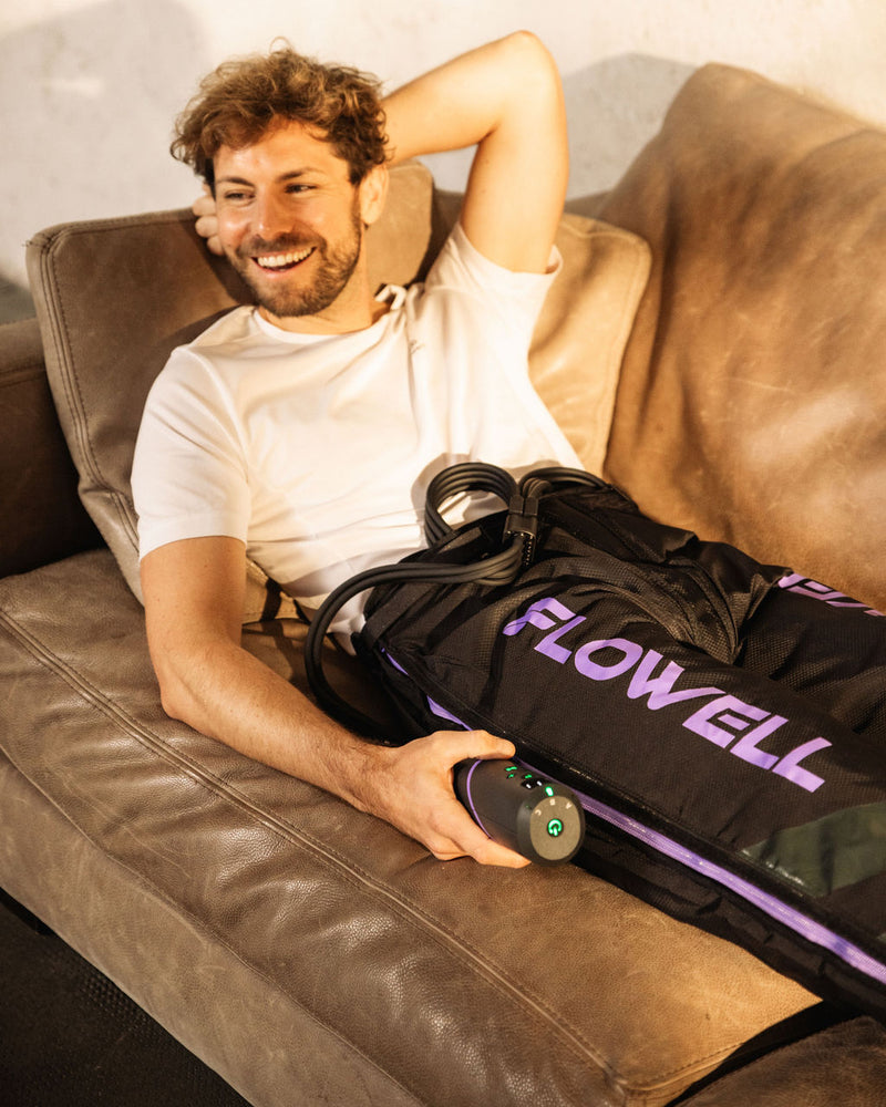 Flowell - Man laying on couch wearing Flowell Sport Mobile Pants, smiling and holding the device's portable control unit