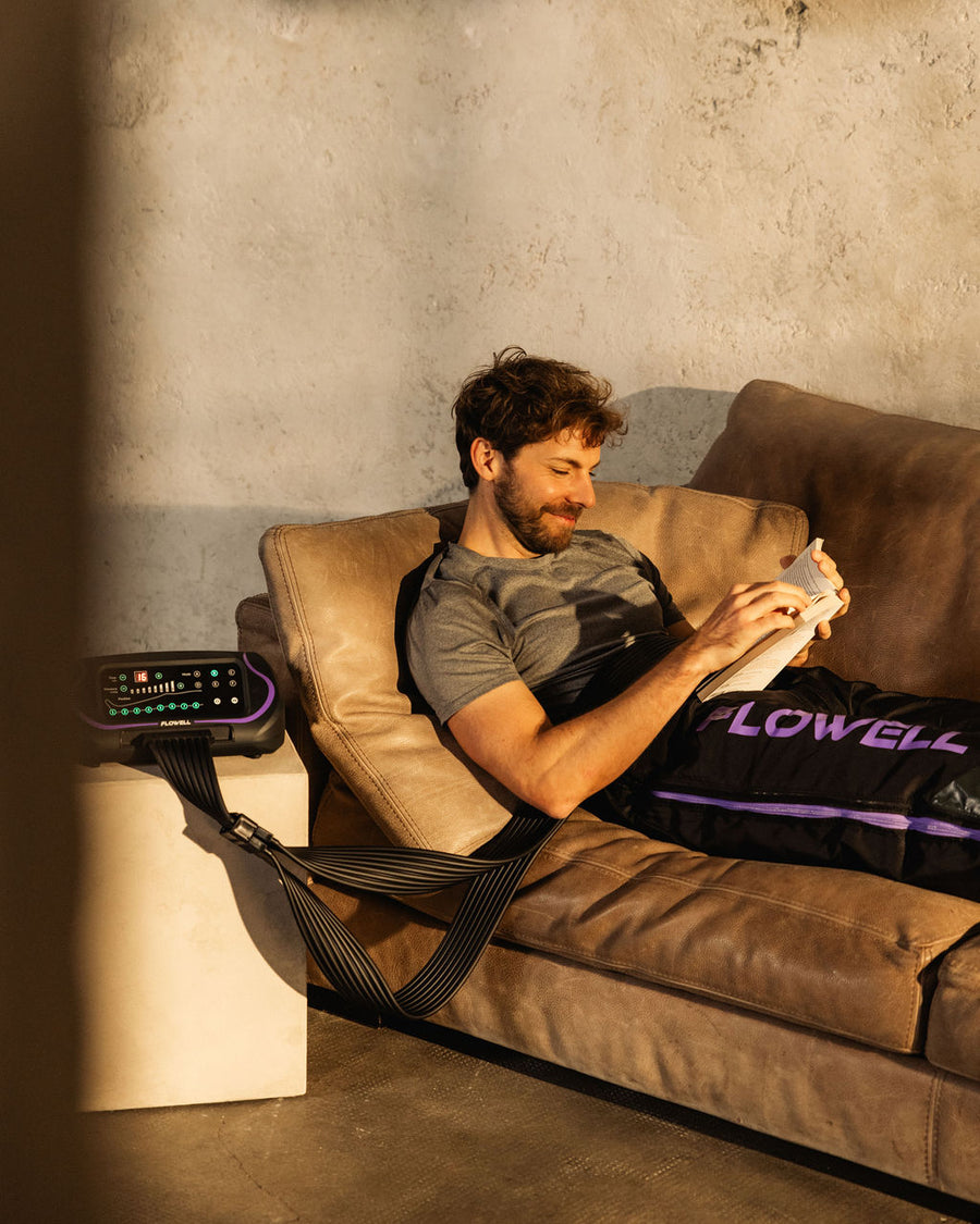 Flowell - Man laying on couch wearing Flowell Sport Deluxe Pants while reading a book with the device control unit by his side