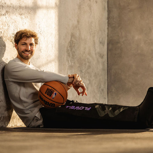 Flowell Sport Mobile Boots Set - Man sitting on the floor using his Flowell Sport Mobile Boots Set in black and purple while holding a basketball. Prioritize recovery with Flowell