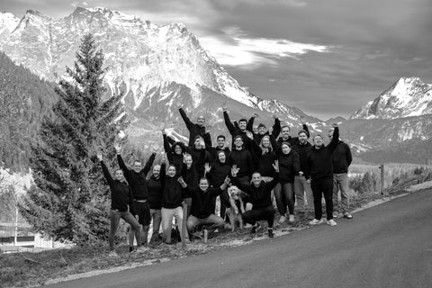 Flowell - Photo of the team smiling, waving and standing at the side of the road at the foot of a tall mountain