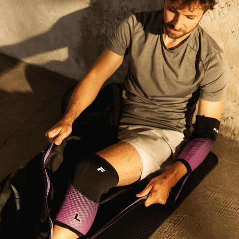 Flowell Thermosleeve - Man wearing purple and black Flowell thermosleeves on his elbow and his knee while putting on his Flowell Mobile Sport Pants