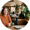 Flowell: Woman sitting at a table in a cozy café, holding a cup.
